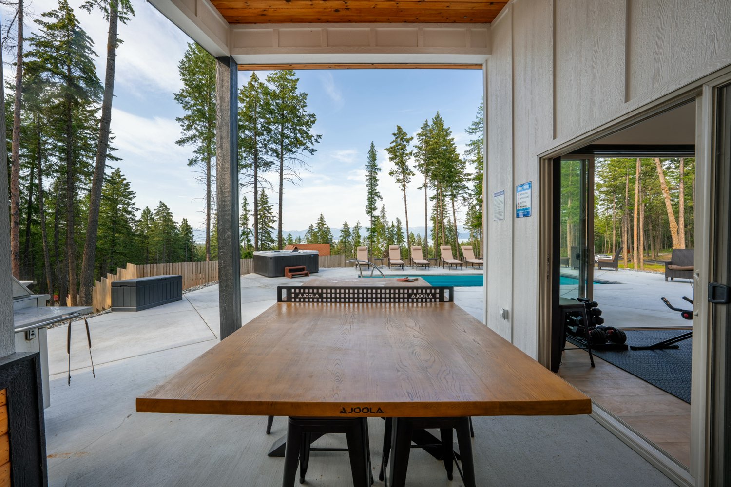 A table tennis table under the pool house's covered deck, looking past the hot tub to the pool and the distant mountains