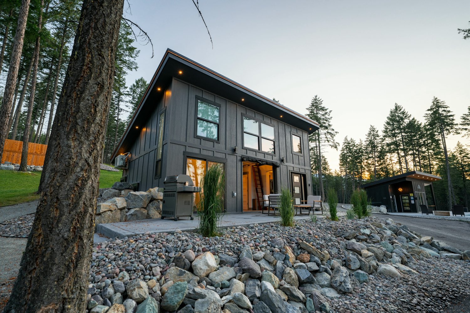 The Glacier House at dusk seen past a ponderosa pine, with its patio, gas grill and the estate drive