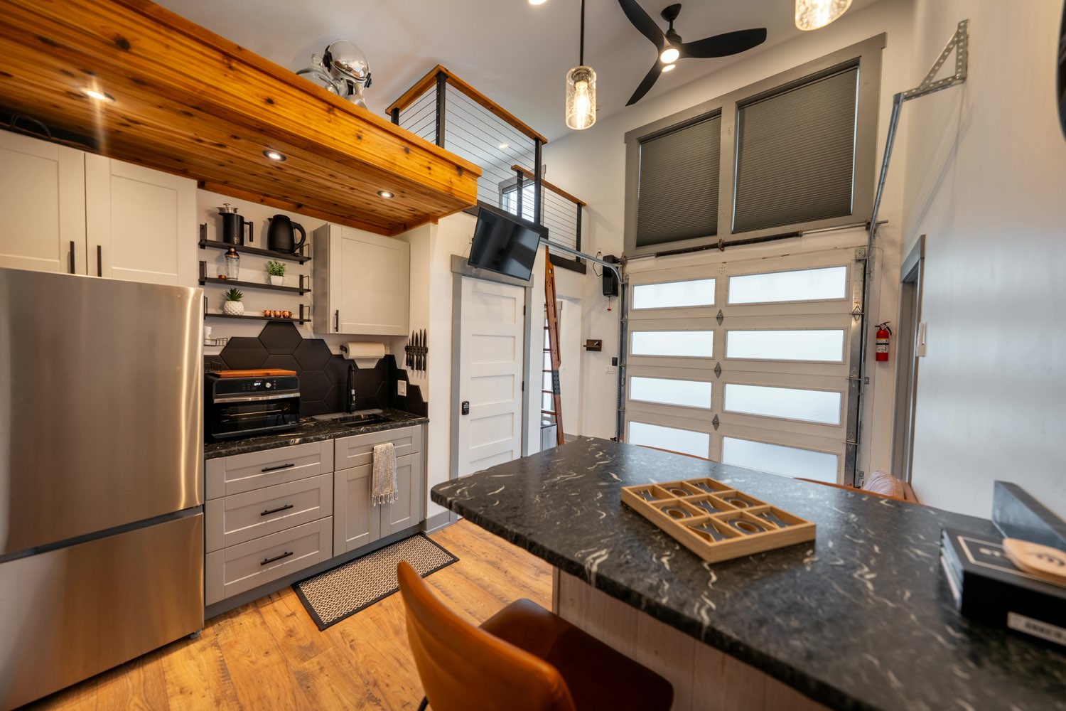 Kitchen at The Glacier House with black stone counters, white cabinetry, a hexagonal tile backsplash and the loft above