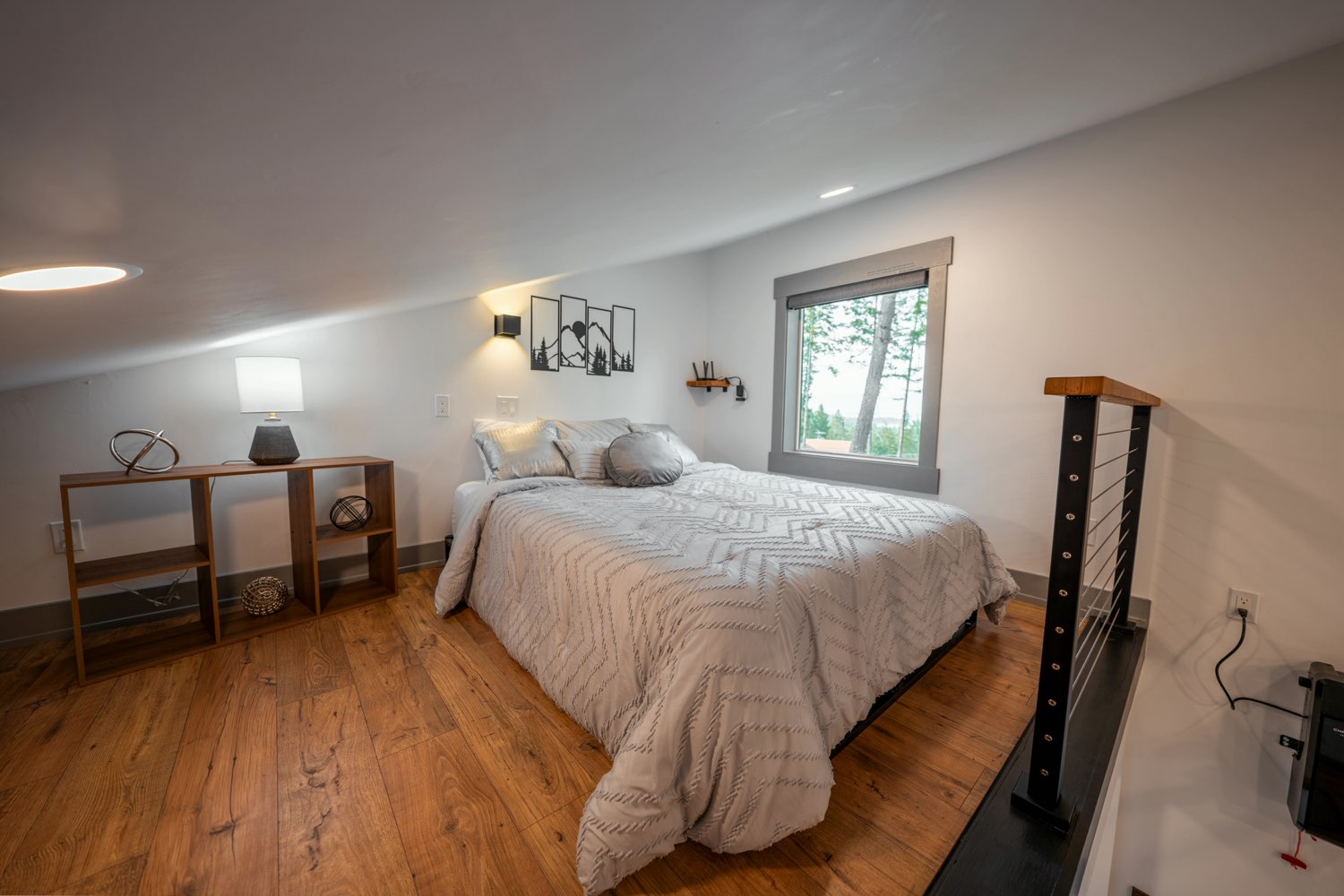 Loft bedroom at The Glacier House beneath the sloped ceiling, with a walnut console and a window onto the pines