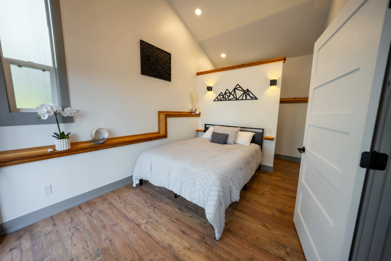 Main bedroom at The Glacier House with mountain-line metal art, wall sconces and a wood ledge running the wall