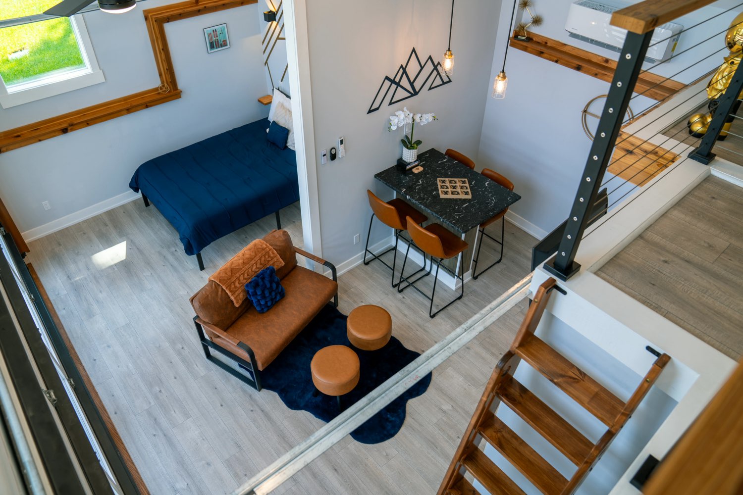 The Lakeside House living area seen from the loft, with a leather loveseat, a bar-height dining table and the bed below