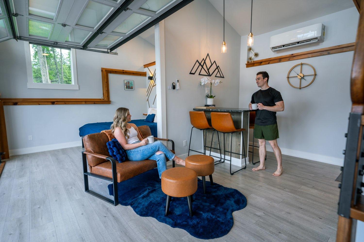 Two guests with coffee in the open-plan living area of The Lakeside House, under the vaulted ceiling beside the ladder to the loft