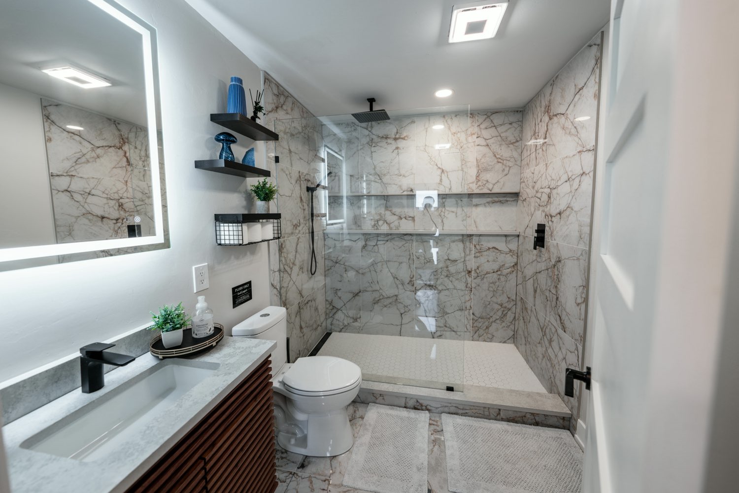 Bathroom at The Lakeside House with a walk-in glass shower, a rainfall head, marble-veined tile and a backlit mirror