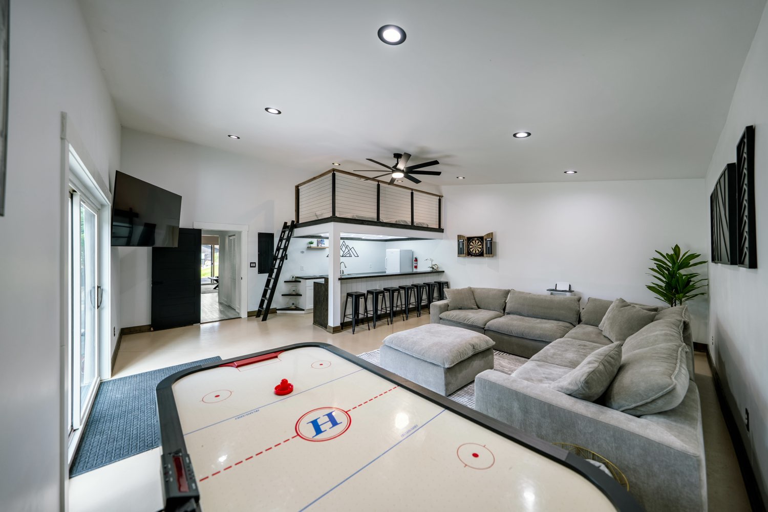 Air hockey table in The Swan House game room, with the sectional, the bar stools and the loft beyond