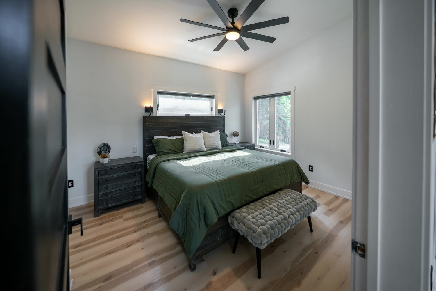 Bedroom at The Swan House with green bedding, a dark plank headboard and a knitted bench at the foot of the bed