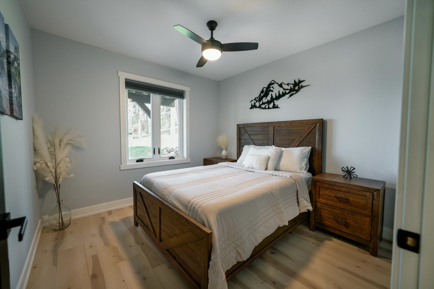 Bedroom at The Swan House with a dark wood bed frame, metal mountain art and a window onto the trees
